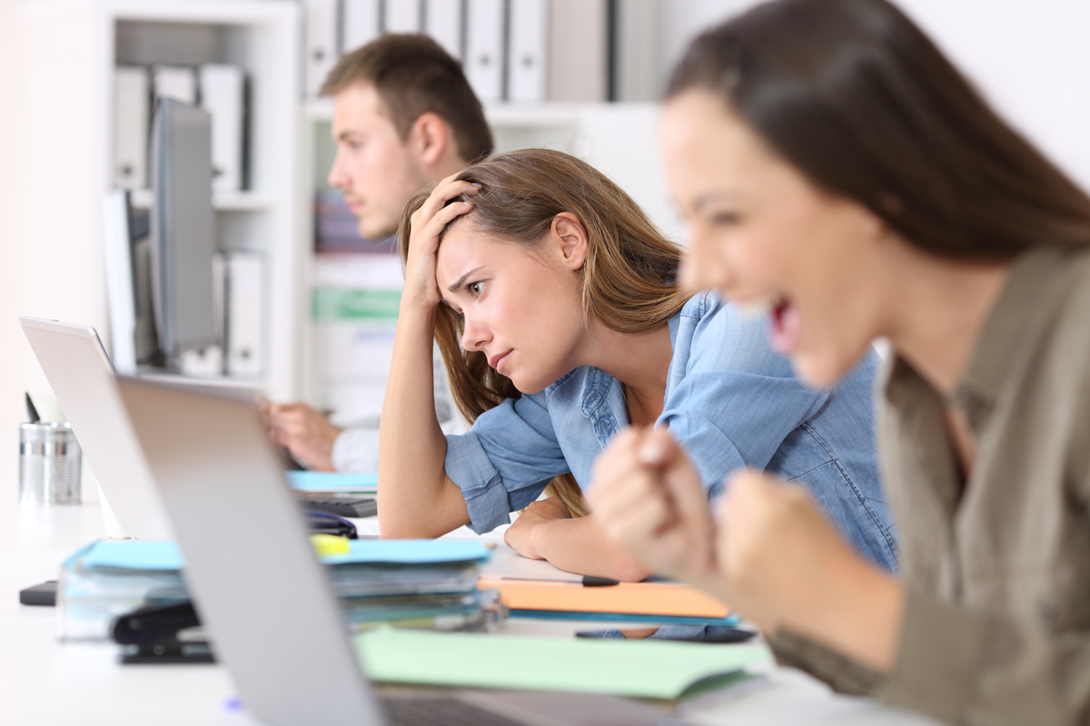 Woman in office looking unhappy while others are happy in the background